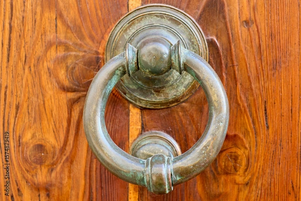 Fototapeta Close-up of an old circular door knocker hanging on a wooden door, showing the texture of the wood and the metal.