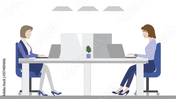 Fototapeta Two women working on laptops at a shared desk in an office with overhead lighting and a small plant