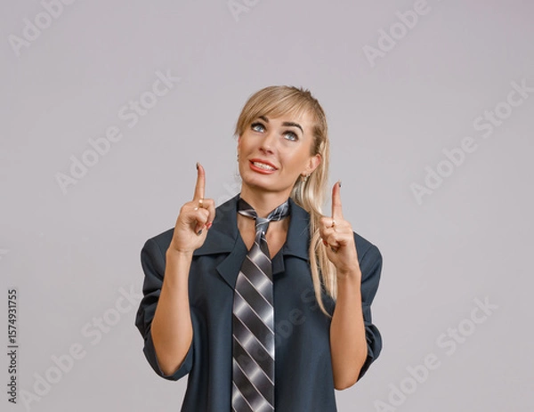 Fototapeta A woman in a dark suit and striped tie pointing upwards with both hands, looking optimistic and interested.