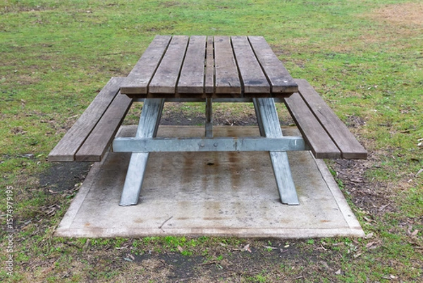 Obraz Photograph of a fixed in place reasonably well maintained family sized wood and steel picnic table with adequate seating located in a large public use campground facility.