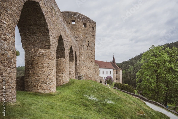 Fototapeta This historic Gothic bridge connects to Velhartice Castle, surrounded by verdant hills. Visitors explore the ancient structure beneath a cloudy sky, immersing in Czech history.