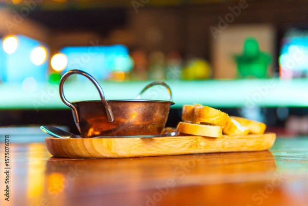Fototapeta A copper bowl with toasted bread sits on a wooden tray in a bar setting.