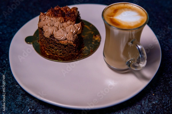 Fototapeta Chocolate cake slice and latte sit invitingly on a plate, ready to be enjoyed.