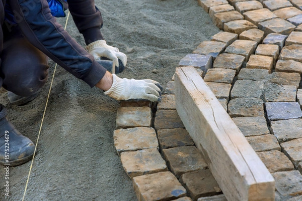 Fototapeta Construction worker carefully placing cobblestones on sandy foundation under works day