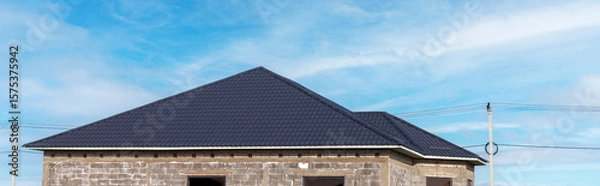 Obraz A house with a metal slate roof and a white wall. The roof is sloping and the house is made of brick.