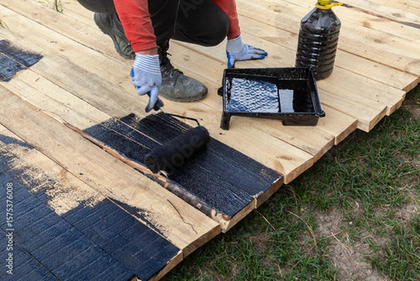 Obraz Man is painting a wooden deck with a roller