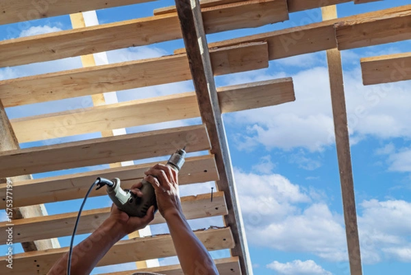 Obraz Builders in work clothes install new roofing tools, roofing tools, electric drill and use them on new wooden roofs with metal sheets