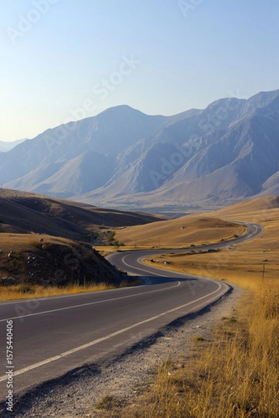 Fototapeta A winding road through a dry landscape with mountains in the background. The scene captures the beauty of nature and the serenity of rural travel.
