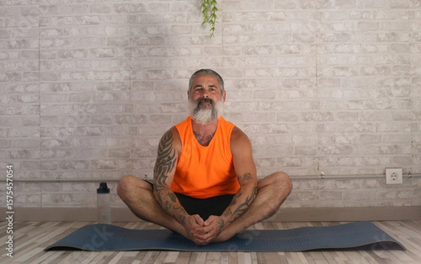 Fototapeta Senior man practicing bound angle pose on yoga mat at home
