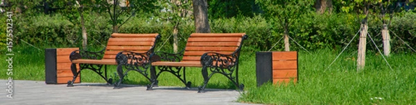 Obraz A charming scene showcasing vintage wooden benches adorned with ornate ironwork, set in a lush city park on a sunny summer day. Photo