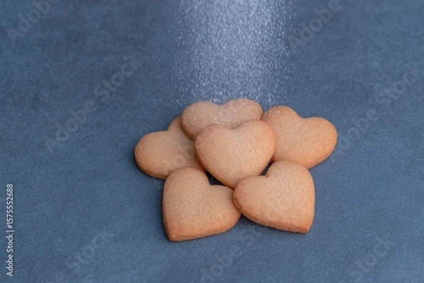 Obraz Delicate heart-shaped cookies being dusted with powdered sugar on a blue surface