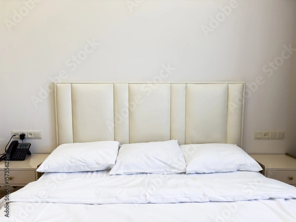 Fototapeta A white bed with a phone on the nightstand. There are three white pillows on the bed