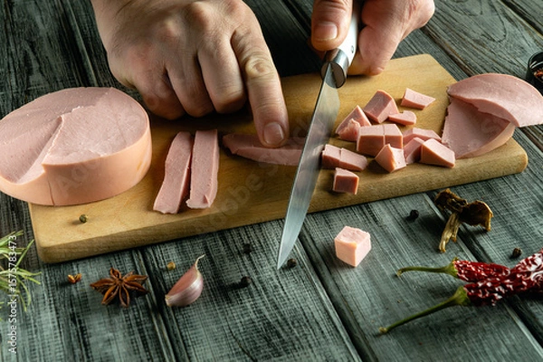 Fototapeta A person skillfully slices deli meats into cubes and strips on a wooden cutting board. Colorful spices and herbs are spread around, enhancing the culinary atmosphere