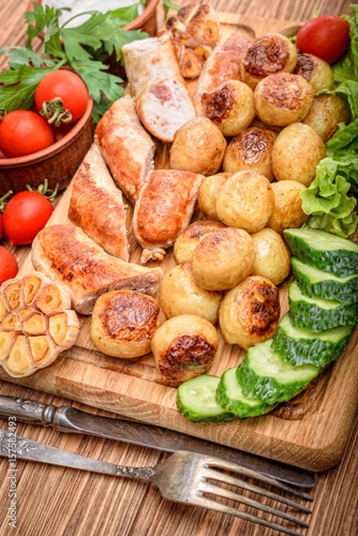 Fototapeta Grilled sausages and vegetables on the wooden board.