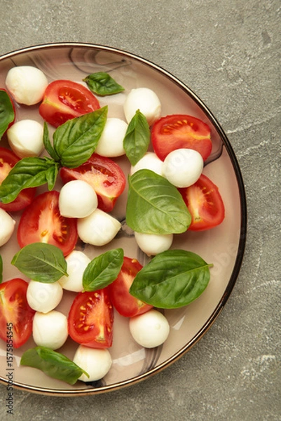 Obraz Italian Caprese salad with cherry tomatoes, mozzarella, basil on plate on grey concrete background. Vertical photo