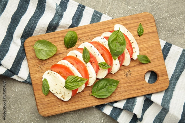 Obraz Mozzarella cheese with green basil leaves and tomato on cutting board on grey background