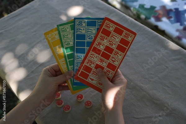 Obraz Lotto game. Outdoors at the table, colorful cards with numbers in the hands of a girl and playing barrels nearby