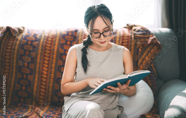 Obraz Beautiful young adult asian woman wearing eyeglasses reading book on sofa relax hobby routines