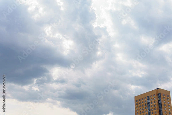 Fototapeta A sky with clouds and a part of a building with windows. The sky occupies most of the frame, while the building is located in the bottom right corner.