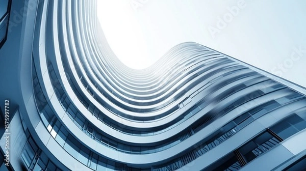 Obraz Low-angle view of a modern, curved skyscraper with numerous balconies and windows, extending towards a bright sky