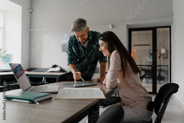 Obraz Two coworkers engaging in a productive discussion while working on a project together.