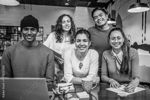 Fototapeta diverse group of young professionals smiling at camera in a modern coworking space. Collaborative multicultural team working on creative project. Black and white image. Diversity concept.
