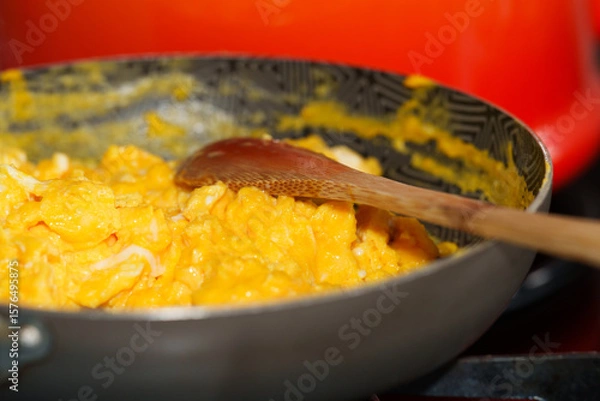 Fototapeta Scrambled eggs being cooked in non-stick frying pan with wooden spoon