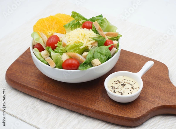 Fototapeta Smoked Chicken Salad, featuring crisp lettuce, cherry tomatoes, shredded cheese, and crunchy croutons in a white bowl with orange slice and creamy dip side view of healthy salad