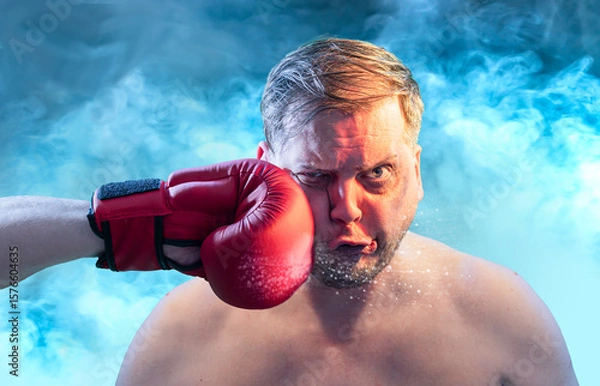 Fototapeta Shocked man getting punched by red boxing glove getting hit in face  with dramatic impact