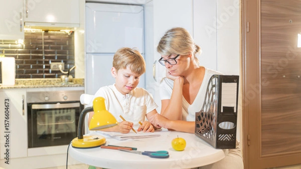 Fototapeta A mother prepares a boy for school and does his homework with him.