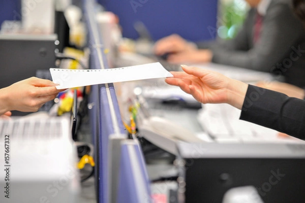 Obraz この書類、頼みます／仕事のイメージ写真で、机のついたて越しに書類はやりとりされる場面