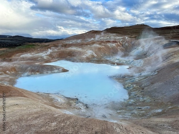 Fototapeta Blue geothermal geysers with steam rising and red mountains in the background, on a Ring Road roadtrip in Iceland