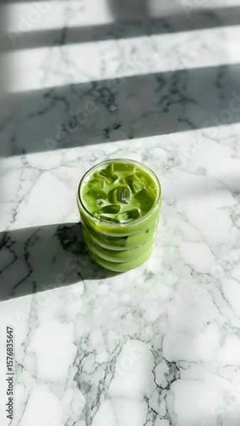 Fototapeta Refreshing Iced Green Drink on a White Marble Surface with Sunlight

