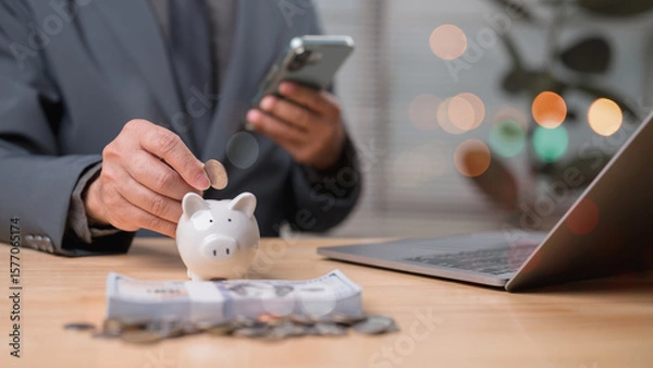Fototapeta Focused Man In Suit Saving Money With Piggy Bank Coin, Financial Planning On Wooden Background With Dollar Bank Elements