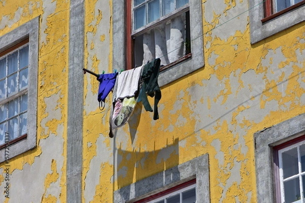 Fototapeta Yellow paint peeling off from plaster facade of weathered town house with laundry hanging in front of window. Location: Porto Portugal