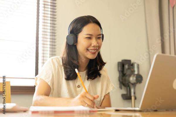 Fototapeta close up young asian woman watch online lecture class on educational website and write on notebook in living room for e-learning education and technology design concept	