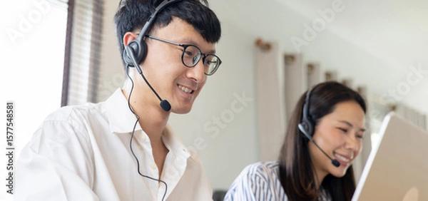 Fototapeta close up asian man call center agent wear headset device and smiling working in operation room with service-mind at desktop table , telemarketing and help desk concept