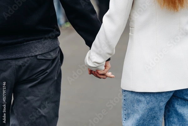 Fototapeta close-up view of couple holding hands, young beautiful caucasian man and woman take each other hands, walking on pathway in park in summer at sunset, love and family concept, selective focus