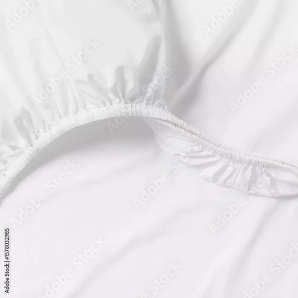 Fototapeta Soft white fitted sheet displayed on a bed, showcasing its smooth texture and elastic edges for a snug fit.