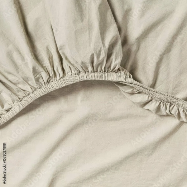 Fototapeta Soft beige fitted sheet with elastic edges displayed on a bed during morning light.