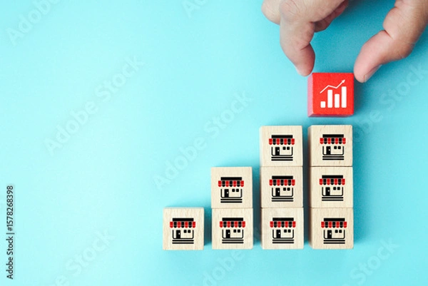 Fototapeta Hand choose wooden block stack with graph and franchise icon for goal to growth is investment planning financial and branch expansion and management bank loans or marketing franchising business.