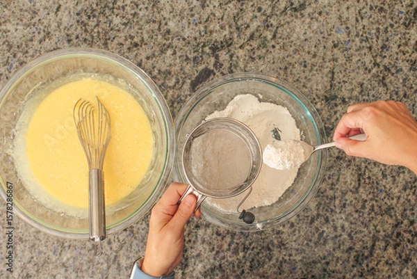 Fototapeta Overhead View of Hands Sifting Flour with Hand Crank Sifter for Baking