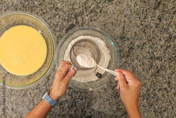 Fototapeta Overhead View of Hands Sifting Flour with Hand Crank Sifter for Baking