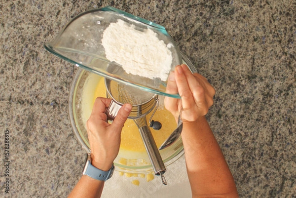 Fototapeta Overhead View of Hands Sifting Flour with Hand Crank Sifter for Baking