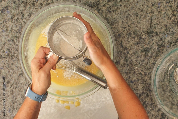 Fototapeta Overhead View of Hands Sifting Flour with Hand Crank Sifter for Baking