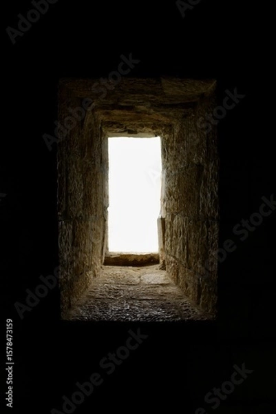 Fototapeta A narrow little window in a thick-walled medieval fortress, like a portal from a dark, musty castle into a clean, bright world.
