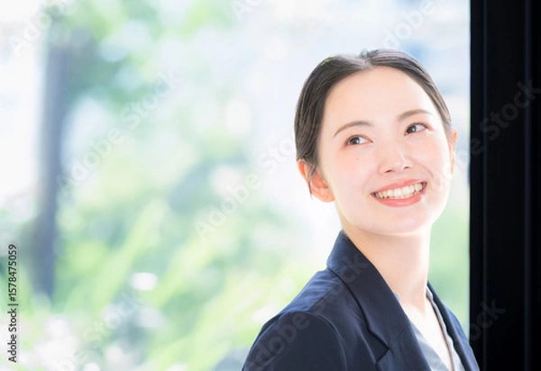 Fototapeta メインビジュアルにも綺麗な柔らかい新緑の中でパソコンを持つスーツの女性のビジネスシーン　クローズアップ　振り返る