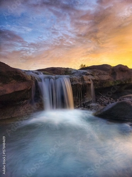 Fototapeta a waterfall that flows between black rocks and is illuminated by the afternoon sun