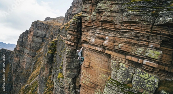 Fototapeta A rock climber ascending a steep, layered cliff face, reaching upwards.