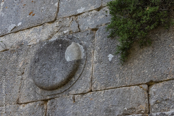 Fototapeta Termessos is an ancient city located in Turkey high in the mountains. The walls of the buildings in the ancient city are made of large smooth stone blocks. A round symbol is carved on the block.